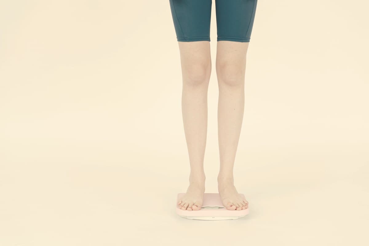 A woman standing calmly near a scale in soft natural light, representing the limits of scale measurements during body recomposition on GLP-1 medication.