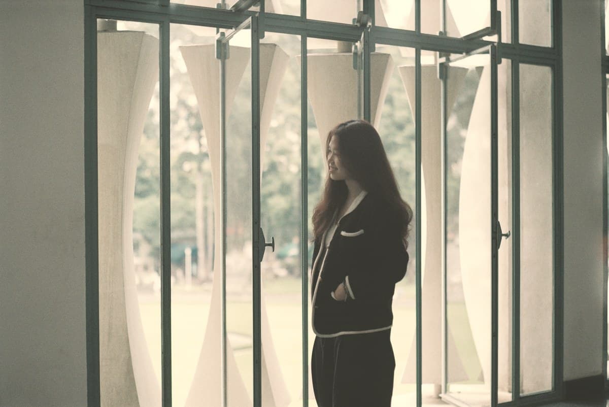 Woman in a dark jacket standing at a tall glass wall, stock photo