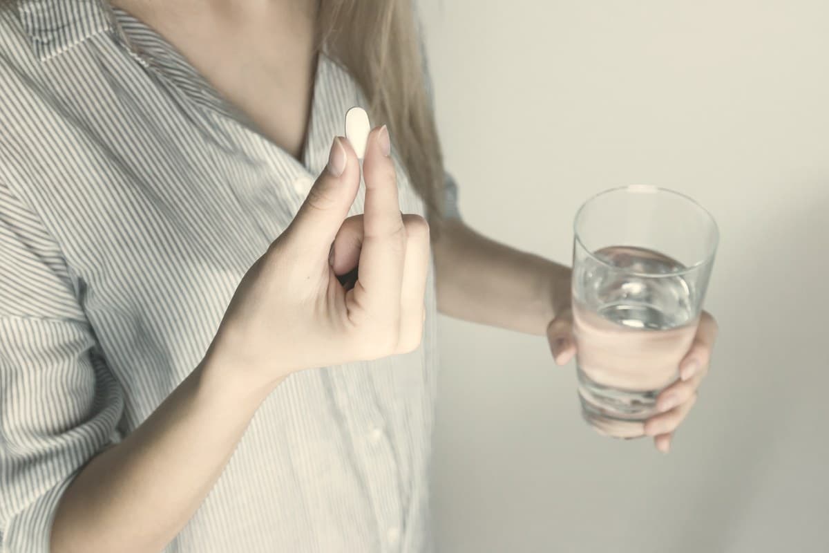 Woman holding a white pill and a glass of water