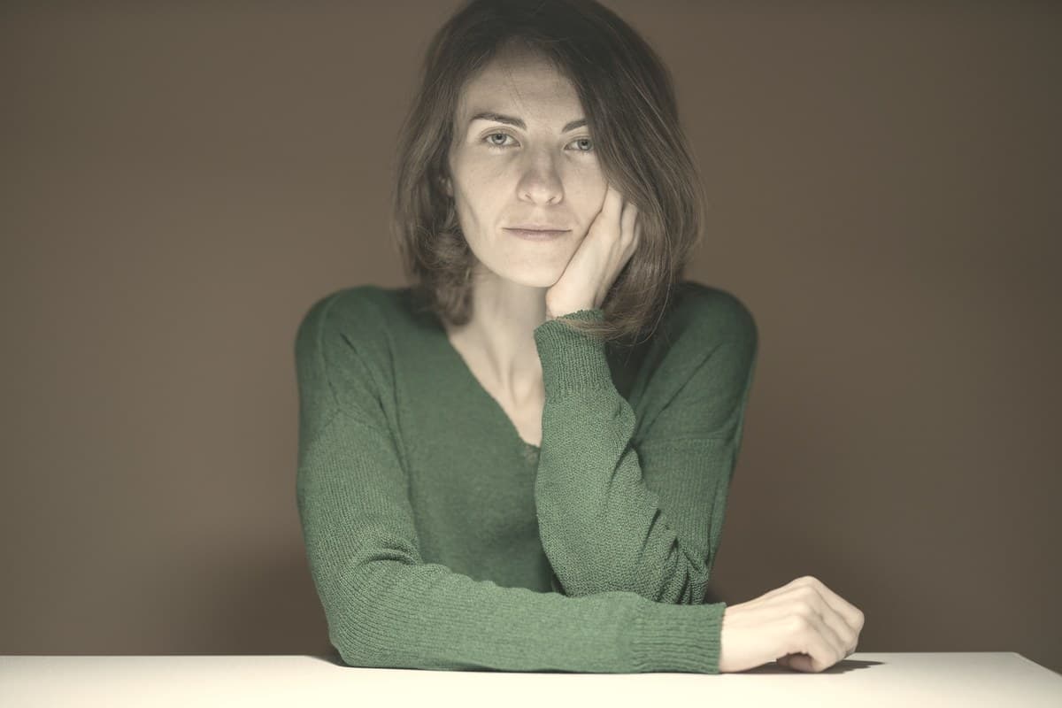 Woman in a green sweater resting her cheek on her hand at a table, stock photo