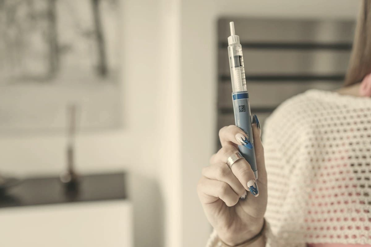 Woman holding a GLP-1 injection pen at home — continuing the medication is the single most effective way to prevent weight regain