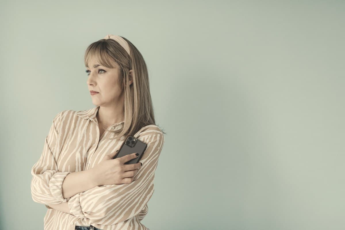 A calm woman glancing at her phone against a plain neutral wall, representing checking the calendar after a missed Ozempic dose