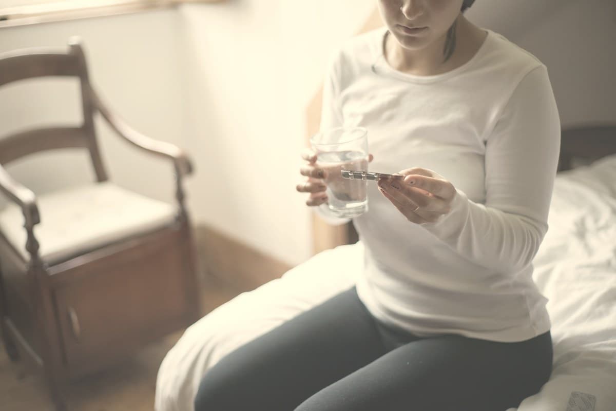 A woman calmly holding a glass of water at a sunlit table, illustrating the daily routine of taking a Wegovy pill dose