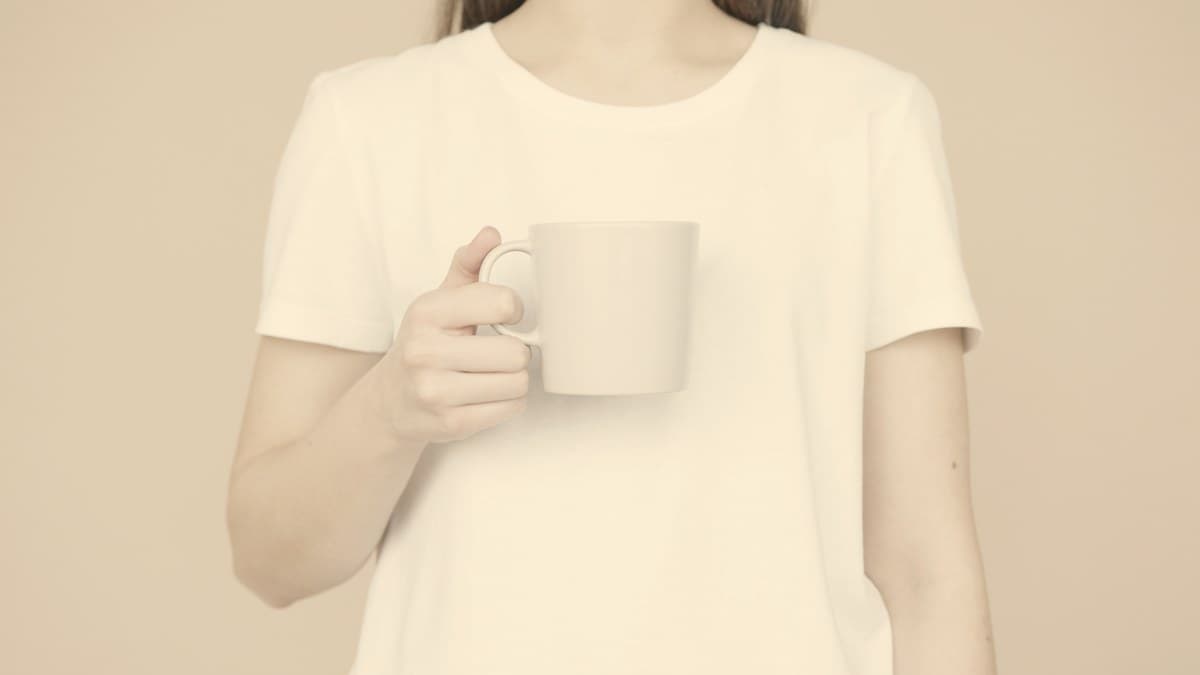 A woman in a white T-shirt holding a plain mug against a soft beige background, a calm morning routine.