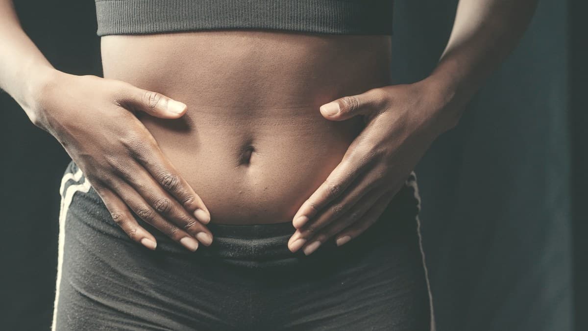 Woman gently touching her abdomen against a soft neutral background, illustrating the primary Ozempic injection site on the stomach.
