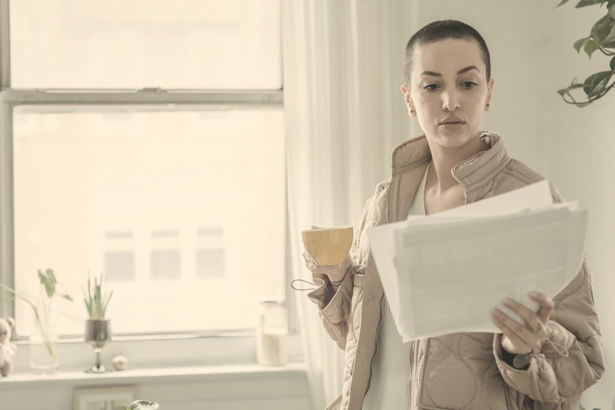 A woman reading printed documents by a window with a cup in her hand, reviewing Zepbound cost and coverage paperwork.