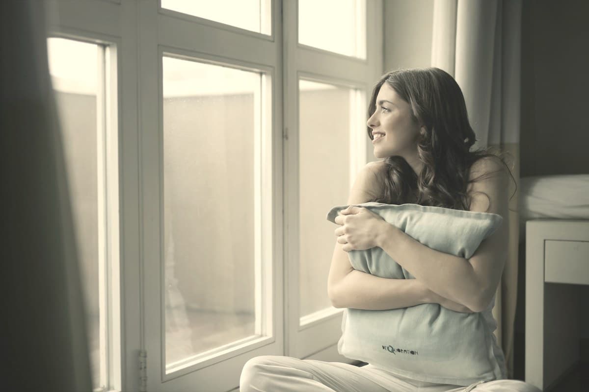 A woman sitting by a window and holding a pillow in soft daylight, resting at home.