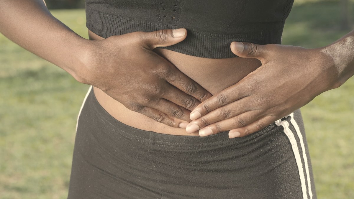 Close-up of a person's midsection with both hands over the stomach — nausea and GI discomfort are the most common GLP-1 side effects during dose escalation