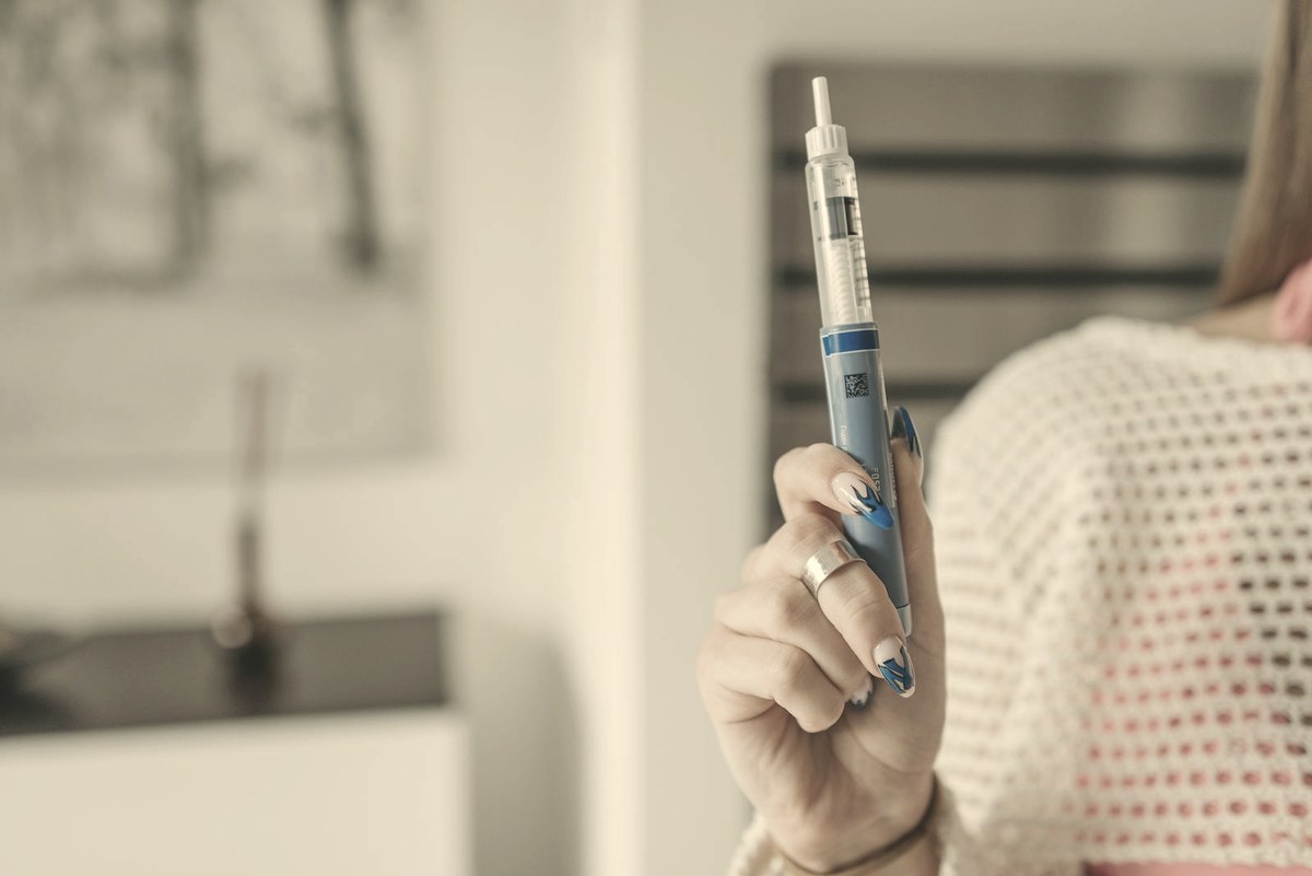Woman holding a GLP-1 injection pen at home — continuing the medication is the single most effective way to prevent weight regain