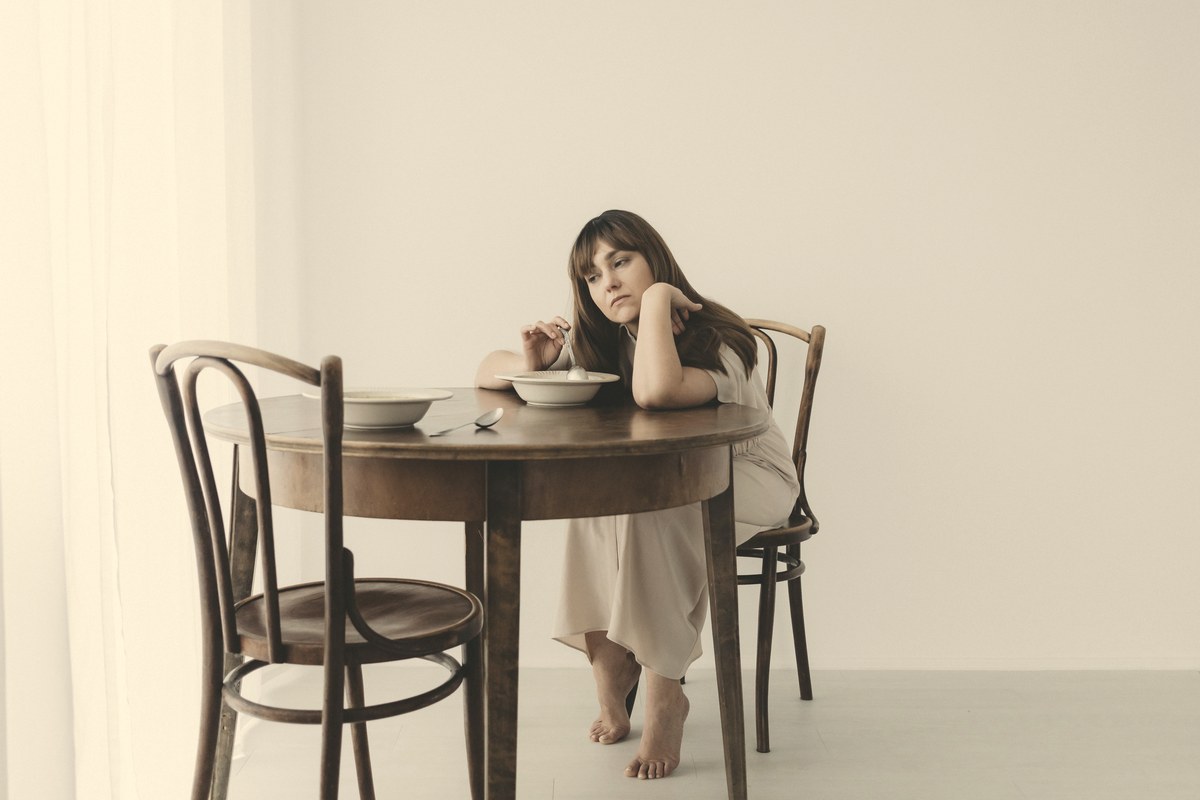 A woman sitting quietly at a minimal table with a small meal, reflecting reduced appetite and mindful eating on GLP-1 therapy