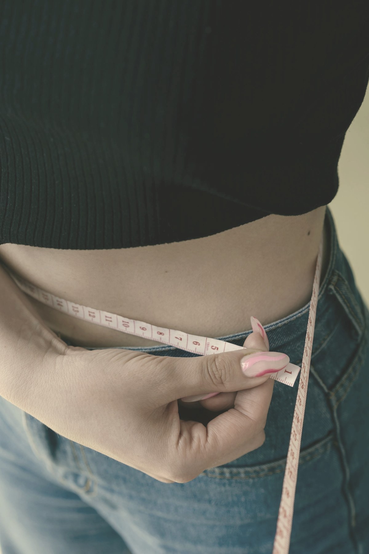 Woman measuring her waist with a tape measure — GLP-1 appetite suppression starts within the first week, but measurable weight loss follows on a slower clock