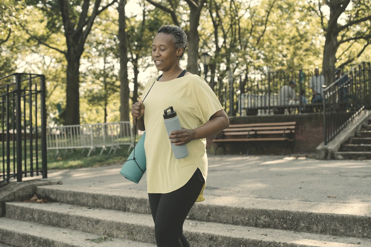 Woman walking outdoors in a park with a yoga mat and water bottle — protein intake and resistance activity protect muscle and metabolic rate during GLP-1 weight loss