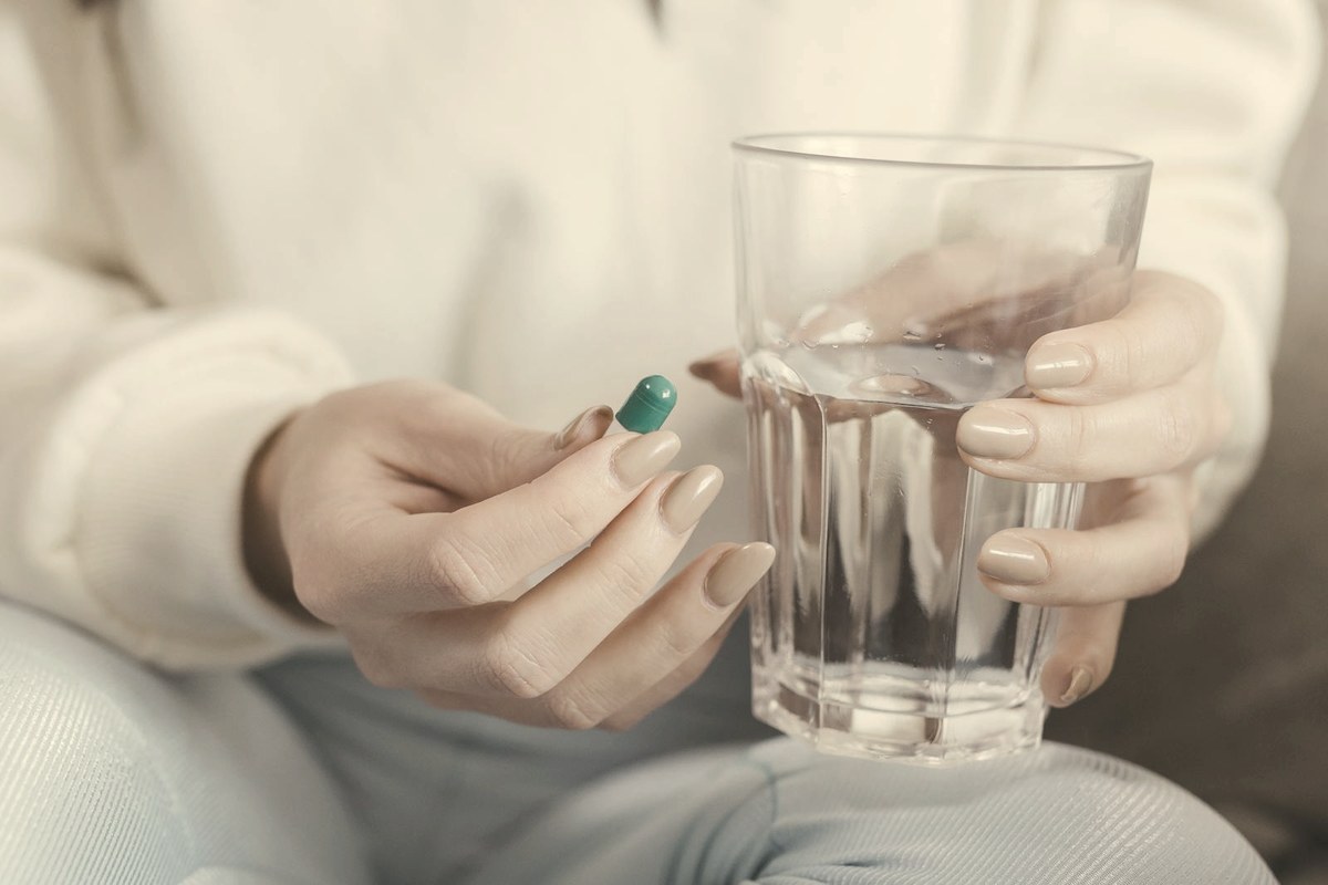 Woman holding an oral medication capsule and a clear glass of water — oral GLP-1 pills now offer a needle-free route to weight loss