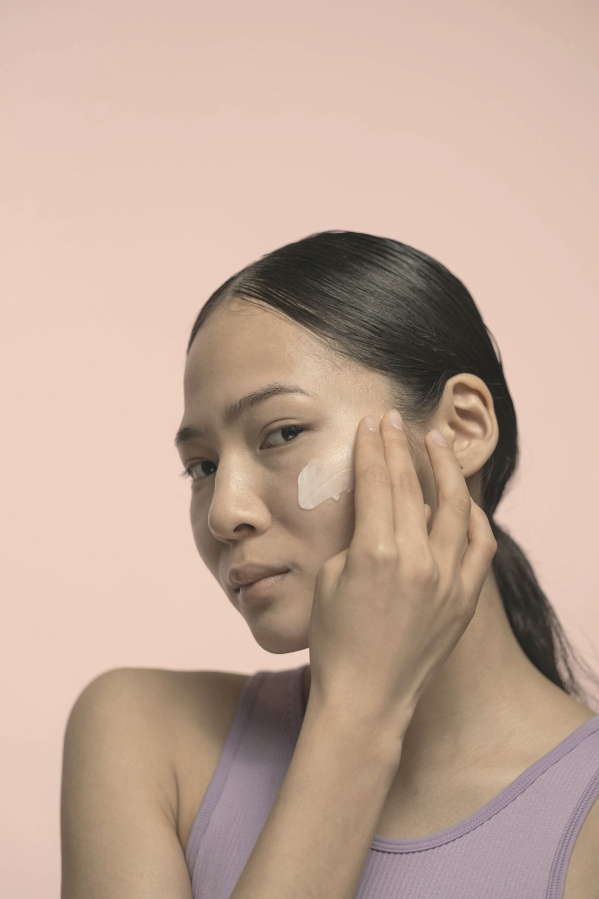 Woman applying moisturizer to her cheek — slower weight loss, protein, and collagen-supporting treatments are the evidence-based responses to Ozempic face