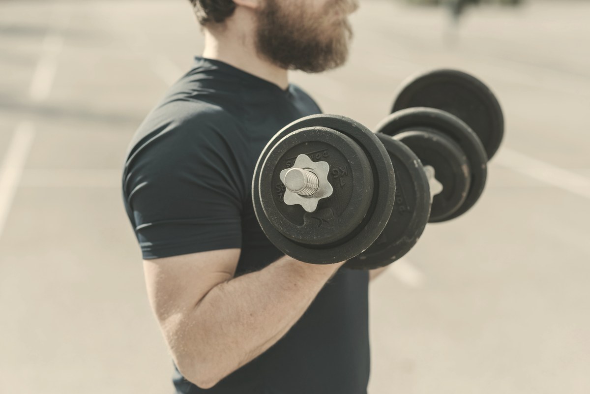 A man curling a dumbbell against a softly blurred neutral background, illustrating the resistance training that preserves muscle on Ozempic.